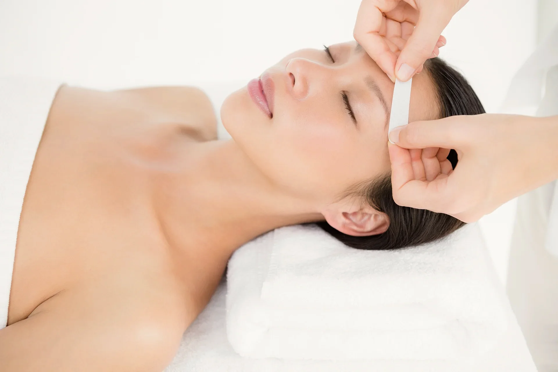 A woman receiving a professional eyebrow waxing and shaping treatment at a beauty spa.
